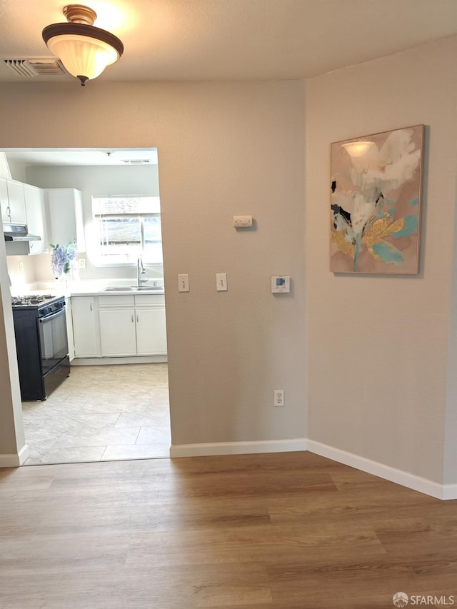 interior space with light wood-type flooring, baseboards, visible vents, and a sink