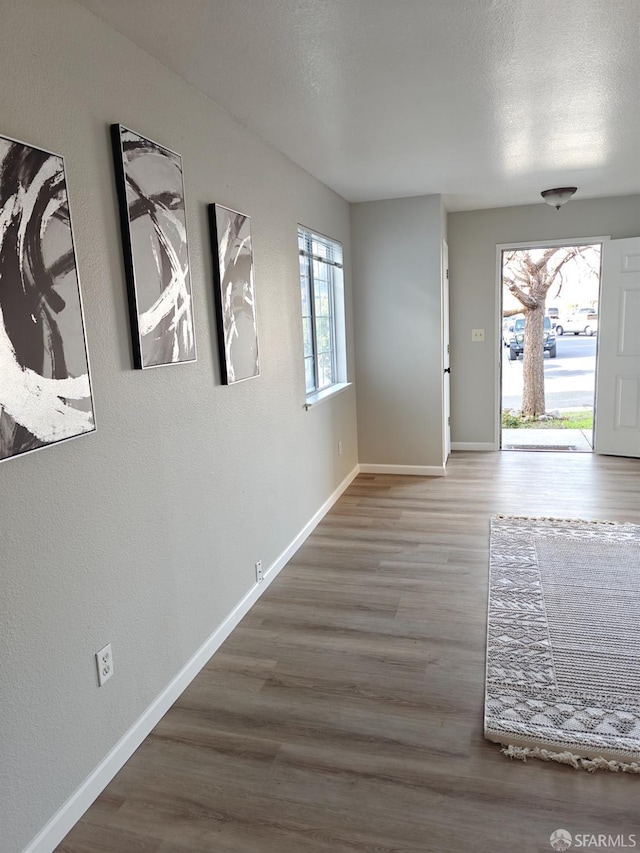 foyer entrance featuring a textured ceiling, baseboards, wood finished floors, and a textured wall