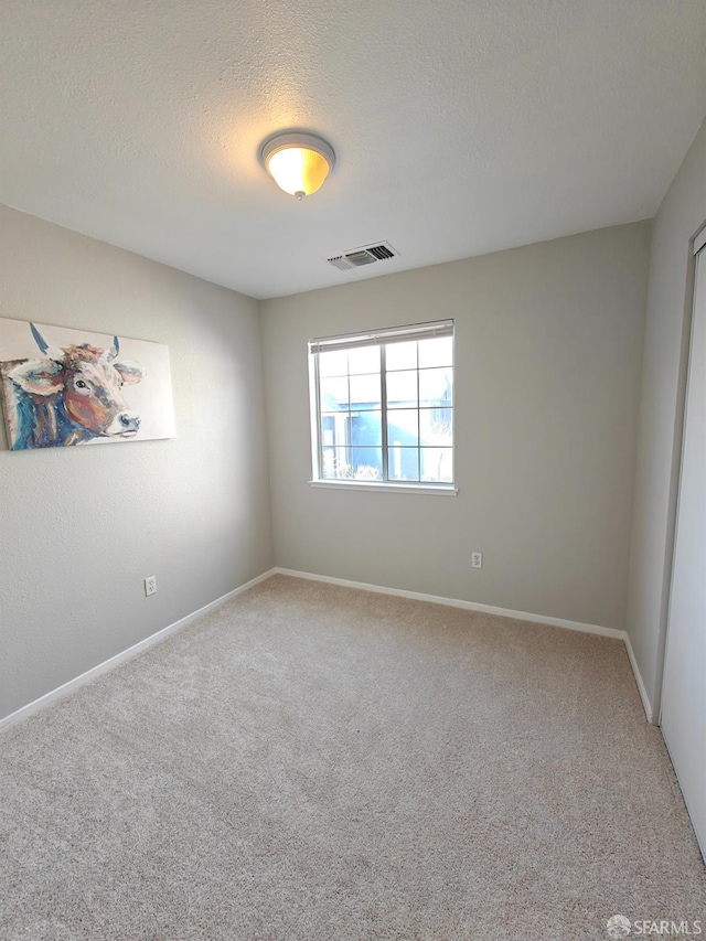 carpeted spare room featuring visible vents, a textured ceiling, and baseboards