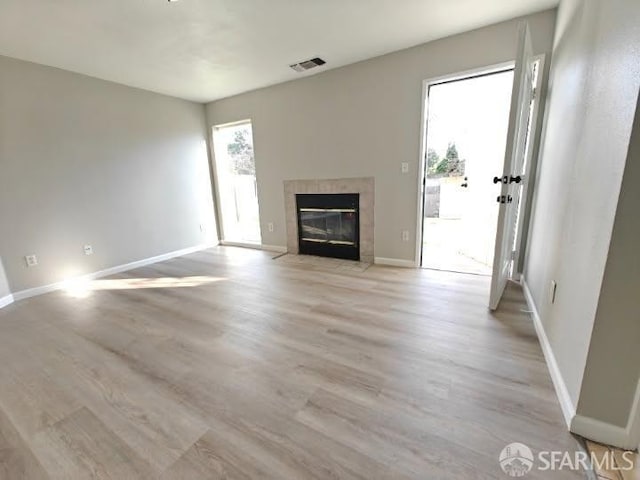 unfurnished living room featuring light wood-style floors, a tile fireplace, visible vents, and baseboards