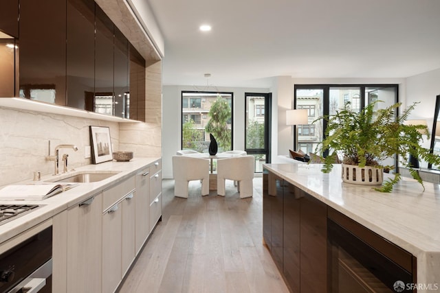 kitchen featuring light hardwood / wood-style flooring, sink, white cabinets, light stone countertops, and decorative backsplash