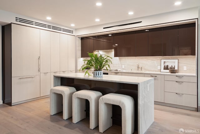 kitchen featuring tasteful backsplash, white cabinetry, a kitchen island, light hardwood / wood-style flooring, and a breakfast bar area