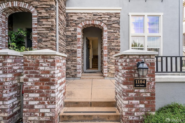 view of exterior entry featuring brick siding and stucco siding