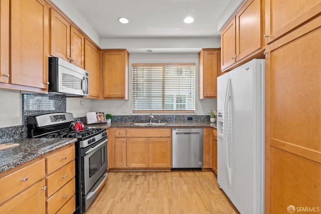 kitchen featuring light wood finished floors, dark stone counters, recessed lighting, a sink, and appliances with stainless steel finishes