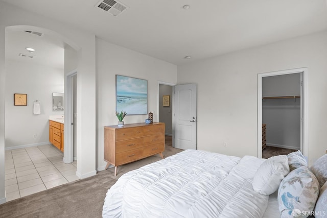 bedroom featuring light tile patterned floors, visible vents, baseboards, arched walkways, and light colored carpet