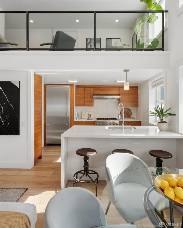 kitchen with sink, built in fridge, light hardwood / wood-style floors, kitchen peninsula, and a breakfast bar area