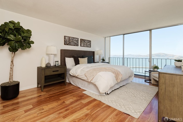 bedroom with hardwood / wood-style flooring, a mountain view, expansive windows, and access to exterior