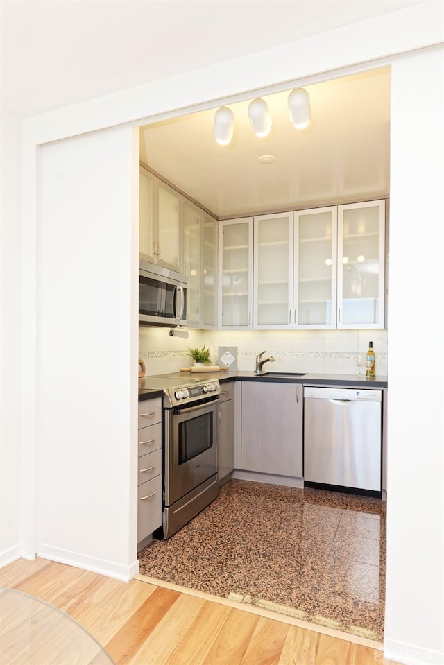 kitchen with backsplash, sink, gray cabinets, light wood-type flooring, and appliances with stainless steel finishes