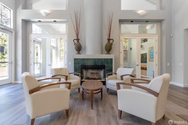 living area featuring french doors, a tiled fireplace, light hardwood / wood-style flooring, and a high ceiling