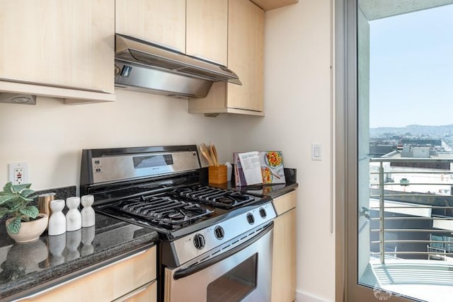 kitchen with dark stone counters, stainless steel gas stove, light brown cabinetry, and ventilation hood