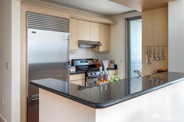 kitchen with light brown cabinetry, dark stone countertops, kitchen peninsula, and appliances with stainless steel finishes