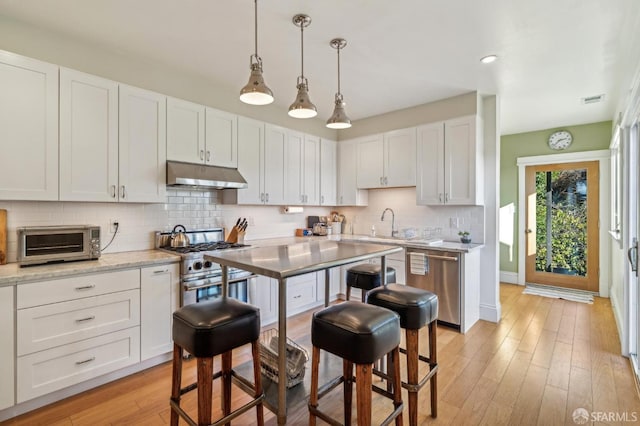 kitchen with stainless steel appliances, white cabinets, light hardwood / wood-style floors, light stone countertops, and pendant lighting