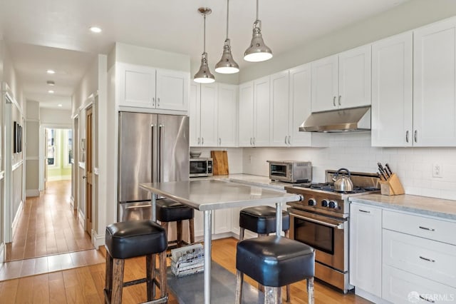 kitchen with light hardwood / wood-style floors, high quality appliances, white cabinets, decorative light fixtures, and backsplash