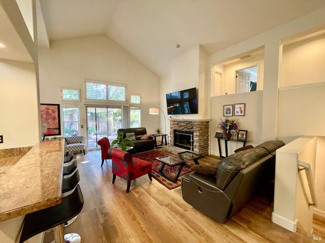 living room featuring high vaulted ceiling, a stone fireplace, and light hardwood / wood-style floors