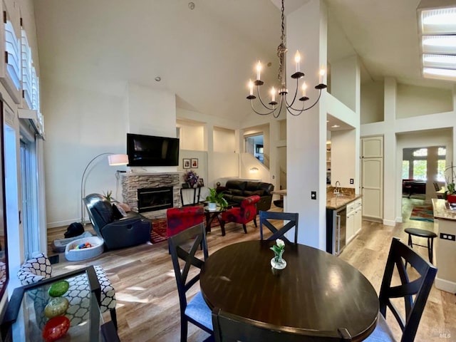 dining area featuring a stone fireplace, sink, high vaulted ceiling, and light wood-type flooring