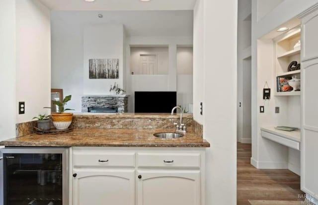 kitchen with sink, light hardwood / wood-style flooring, dark stone countertops, beverage cooler, and white cabinets