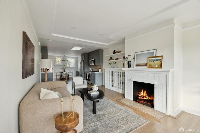 living room with a tiled fireplace, a tray ceiling, light hardwood / wood-style flooring, and ornamental molding