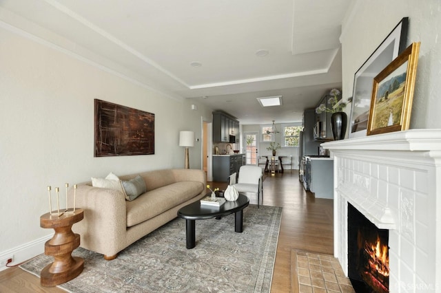 living room featuring hardwood / wood-style flooring, a tray ceiling, a tile fireplace, and a notable chandelier