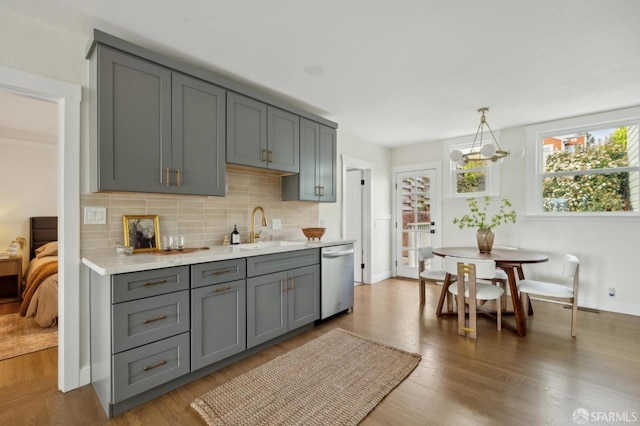 kitchen with sink, hanging light fixtures, stainless steel dishwasher, gray cabinets, and decorative backsplash