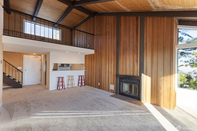 unfurnished living room featuring wooden ceiling, beamed ceiling, wooden walls, and high vaulted ceiling