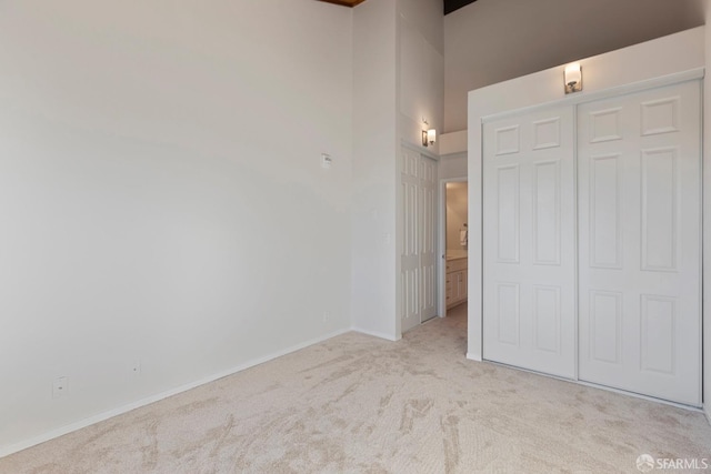 unfurnished bedroom with a closet, light colored carpet, and a high ceiling