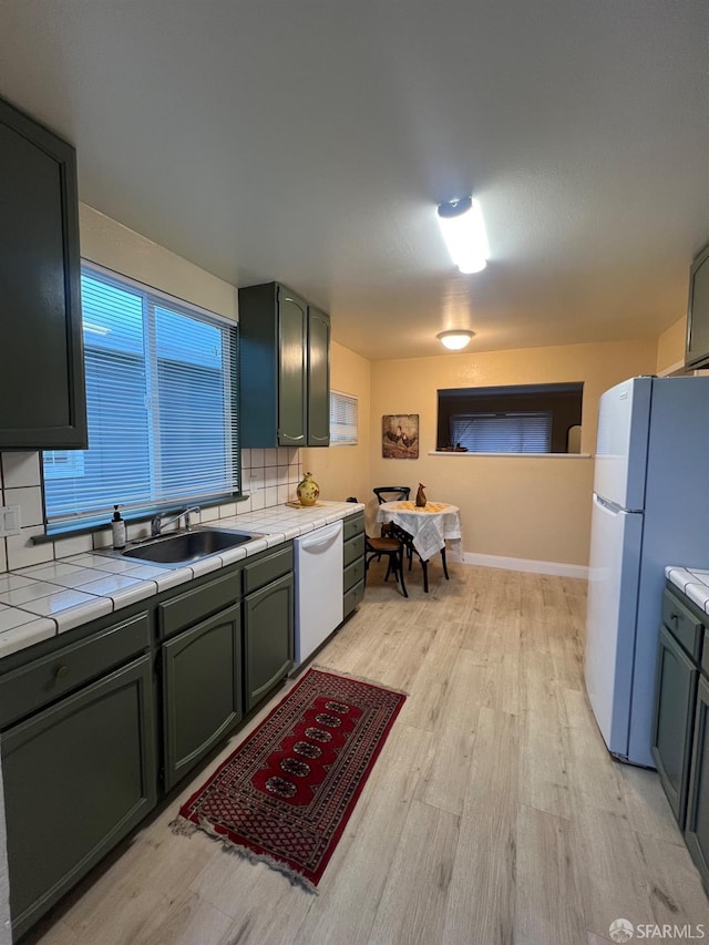 kitchen featuring light wood-style flooring, tile countertops, a sink, and white appliances