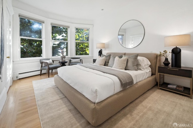 bedroom with light hardwood / wood-style floors and a baseboard heating unit