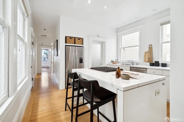 kitchen featuring appliances with stainless steel finishes, a kitchen island, sink, light hardwood / wood-style flooring, and white cabinetry