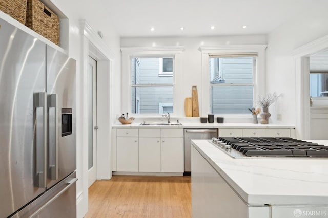 kitchen featuring sink, light hardwood / wood-style flooring, light stone countertops, appliances with stainless steel finishes, and white cabinetry