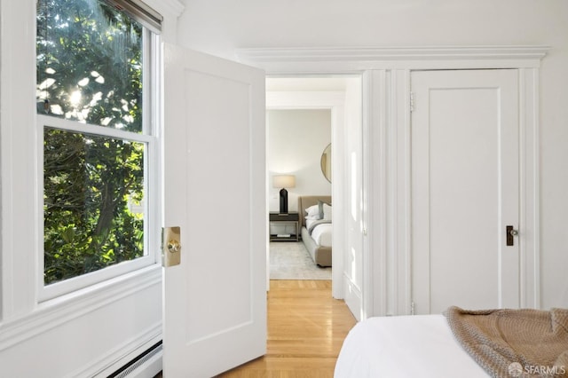 bedroom with light hardwood / wood-style floors, crown molding, baseboard heating, and multiple windows