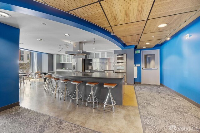 kitchen featuring stainless steel appliances, island exhaust hood, dark countertops, and baseboards