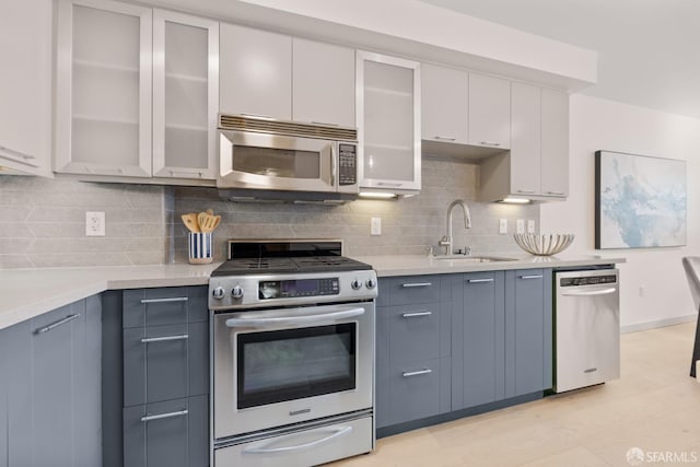 kitchen featuring appliances with stainless steel finishes, a sink, light countertops, decorative backsplash, and glass insert cabinets