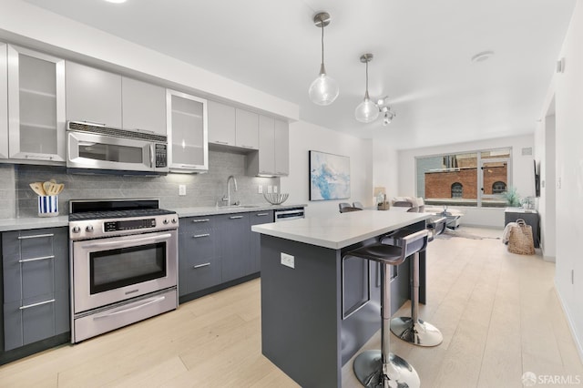 kitchen with stainless steel appliances, gray cabinets, a sink, tasteful backsplash, and light countertops
