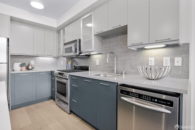 kitchen featuring appliances with stainless steel finishes, a sink, light countertops, decorative backsplash, and glass insert cabinets