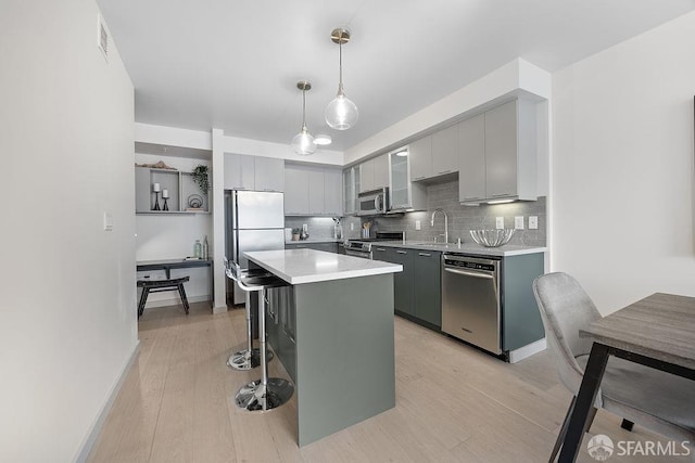 kitchen with appliances with stainless steel finishes, gray cabinetry, a kitchen bar, and light wood-type flooring