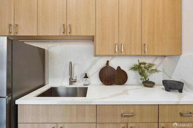 kitchen featuring stainless steel refrigerator, sink, decorative backsplash, light stone countertops, and light brown cabinets