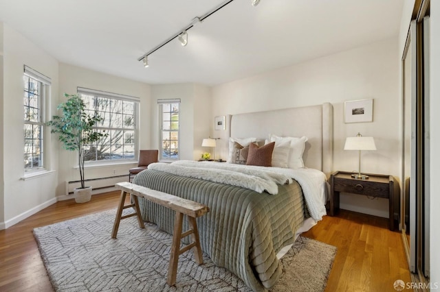 bedroom featuring a baseboard radiator, wood-type flooring, rail lighting, and multiple windows