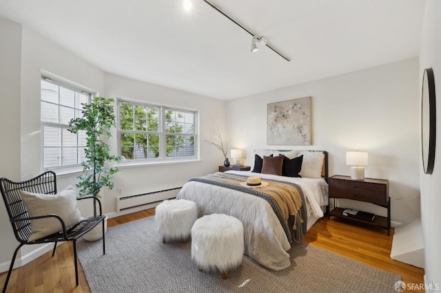 bedroom featuring baseboard heating, wood-type flooring, and rail lighting