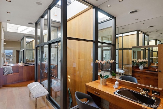 bathroom featuring a skylight, visible vents, wood finished floors, vanity, and floor to ceiling windows