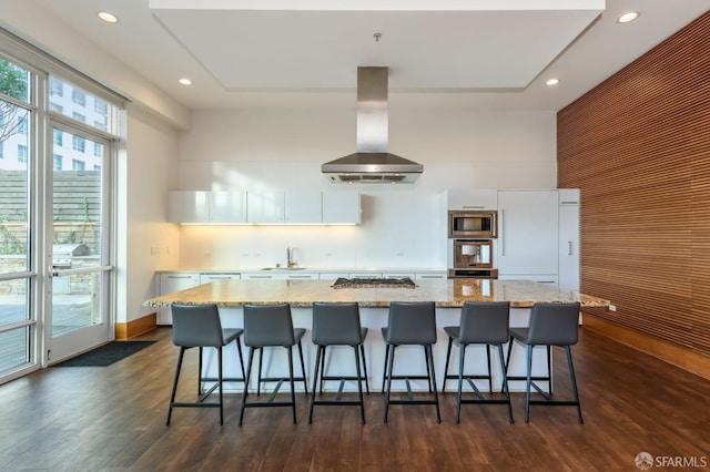 kitchen featuring appliances with stainless steel finishes, white cabinetry, a center island with sink, and exhaust hood