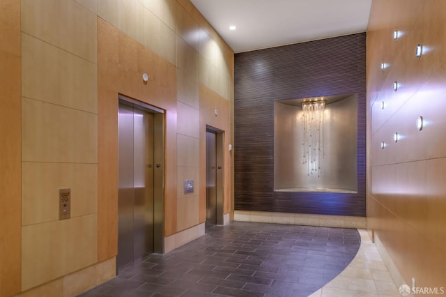 hall with tile walls, a high ceiling, and elevator