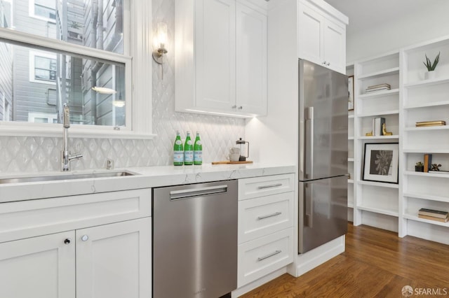 kitchen with stainless steel appliances, a sink, white cabinets, decorative backsplash, and dark wood finished floors