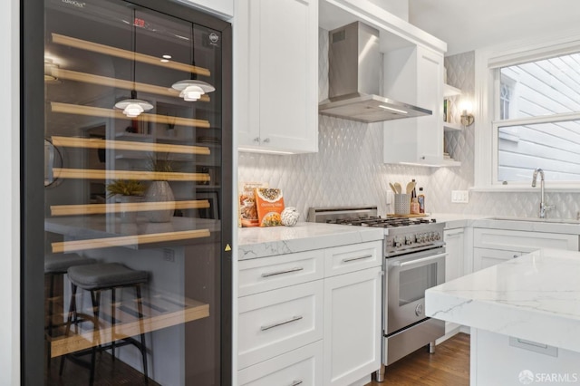 kitchen featuring high end stove, beverage cooler, a sink, white cabinetry, and wall chimney range hood