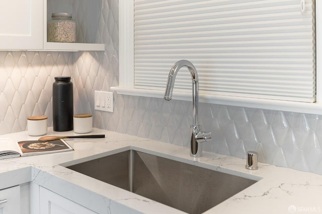 details with light stone counters, white cabinetry, a sink, and decorative backsplash