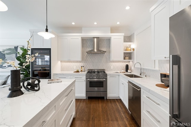 kitchen featuring white cabinets, appliances with stainless steel finishes, a sink, wall chimney range hood, and backsplash