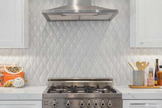 kitchen with white cabinets, decorative backsplash, stove, light stone countertops, and wall chimney range hood