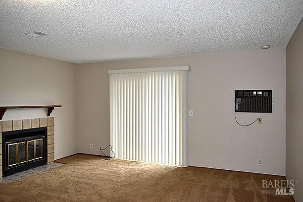 unfurnished living room featuring visible vents, carpet, a wall unit AC, a fireplace, and a textured ceiling