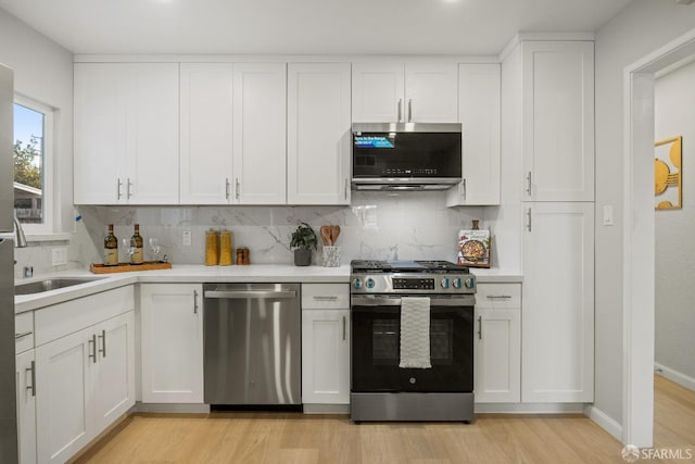 kitchen featuring stainless steel appliances, light wood-type flooring, sink, white cabinetry, and tasteful backsplash