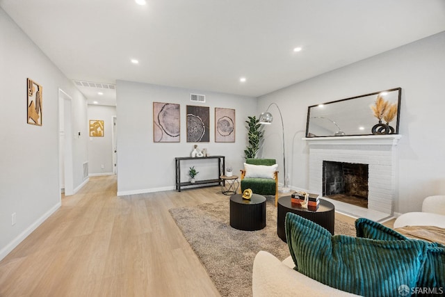 living room with a brick fireplace and light wood-type flooring