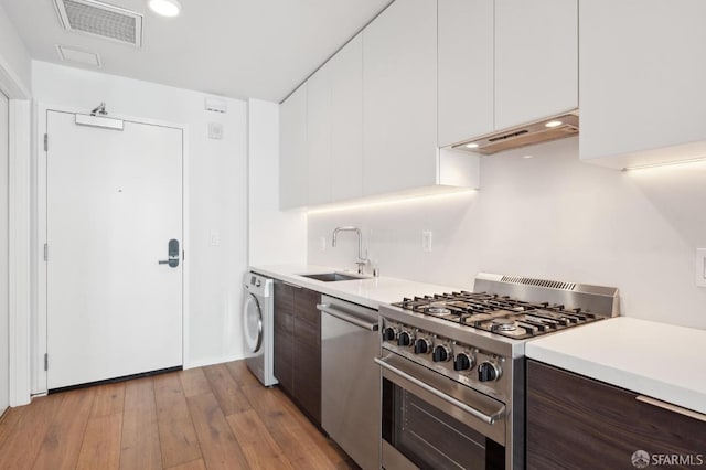 1433 Bush St Unit 702, San Francisco, CA 94109 - kitchen featuring white cabinets, extractor fan, stainless steel appliances, washer / dryer, and light wood-type flooring